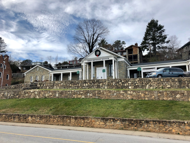 Steinwand mit geparkten Autos, angrenzende Gebäude mit Fenstern und Türen, Bäume und ein bewölkter Himmel, als Weltkulturerbe-Museum bezeichnet.