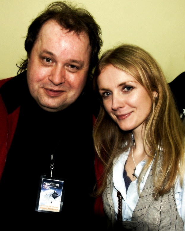 Ein Mann und eine Frau lächeln mit einem sichtbaren Abzeichen vor einem hellgelben Hintergrund.