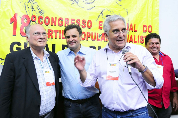 Ein Mann spricht in ein Mikrofon vor einem gelben Vorhang mit der Aufschrift "18. Kongress o."