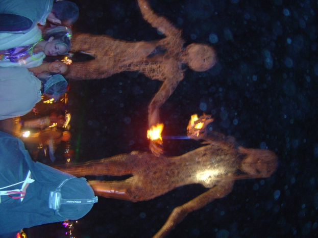 Menschen vor brennenden Statuen mit Lichtern im Hintergrund