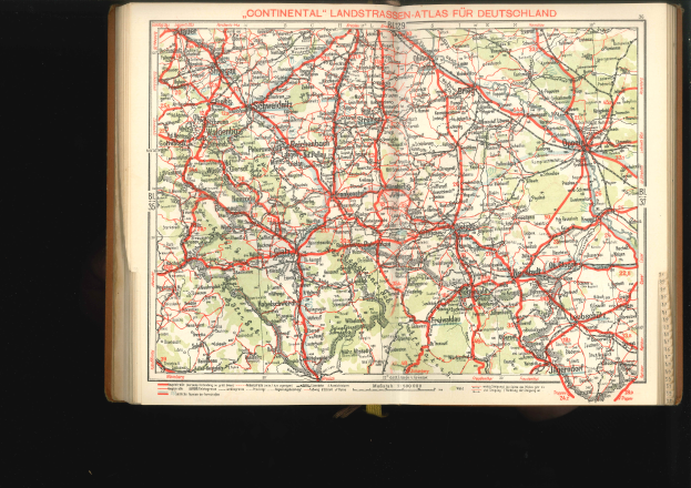 Ein aufgeschlagenes Buch mit einer detaillierten Deutschlandkarte mit Straßen und Autobahnen auf einem schwarzen Hintergrund.