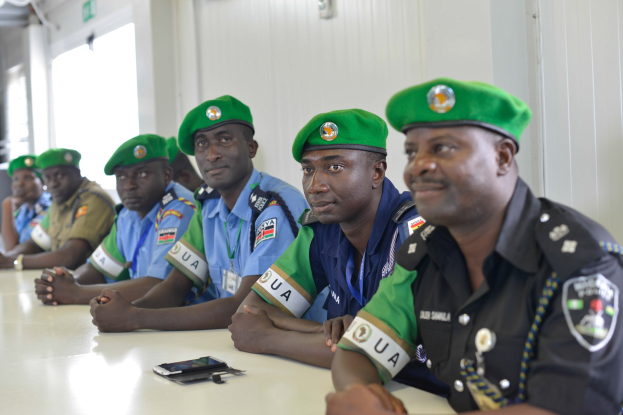 Gruppe von Polizeibeamten, die während einer Schulung an einem Tisch sitzen, mit Mobiltelefonen und anderen Gegenständen auf dem Tisch, in einem Raum mit Fenstern und Deckenbeleuchtung.