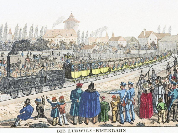Eine Gruppe von Menschen um einen Zug auf Schienen herumstehend, einige sitzen im Zug und andere auf dem Boden, vor Gebäuden und Bäumen im Hintergrund, mit Text 'Ludwigs-Eisenbahn, der erste Bahnhof in Deutschland' unten.