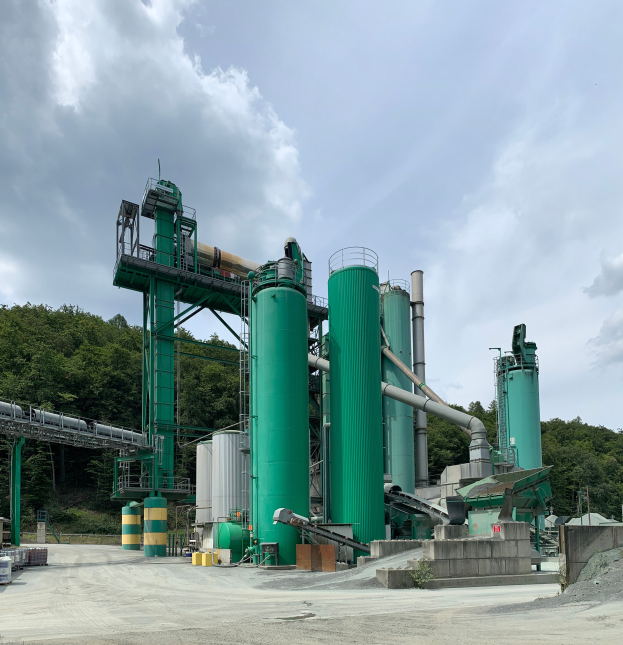 Eine große industrielle Müllreifen-Pyrolyseanlage mit zahlreichen grünen Tanks, Maschinen und Polen, vor einem Hintergrund aus Bäumen und einem bewölkten Himmel.