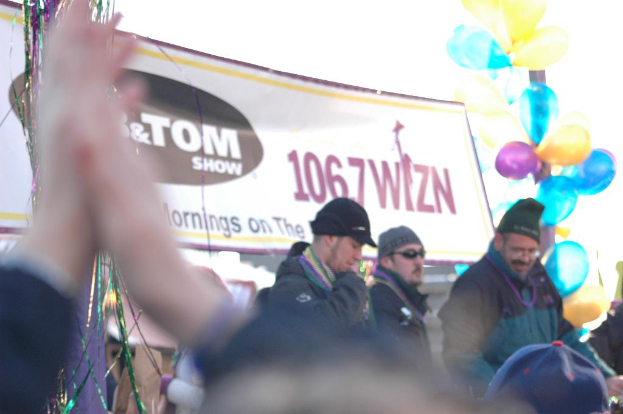 Menschen mit Mützen stehen zusammen, mit Ballons an einem Eisenpfahl und bunten Glitzerdraht in der Nähe.