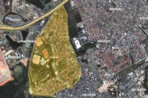 Eine Luftaufnahme einer Stadt mit Gebäuden, Straßen und Grünflächen, die eine zentrale Karte eines geplanten Entwicklungsgebiets zeigt.