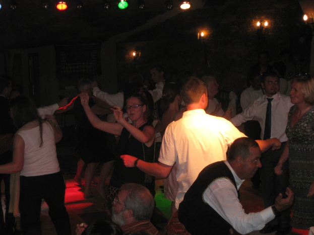 Eine lebendige Partyszene mit tanzenden Menschen auf der Tanzfläche unter verschiedenen farbigen Lichtern in einem dunklen Raum.