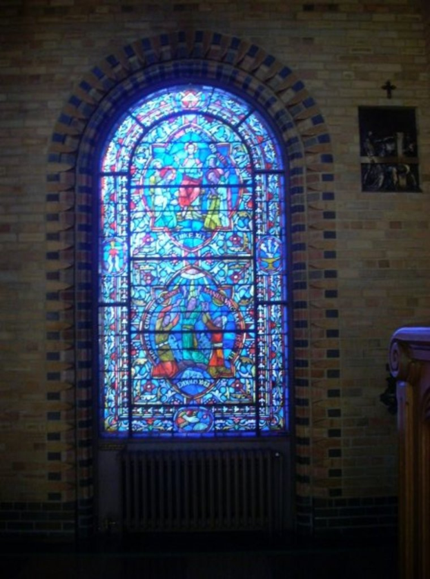 Ein Blick ins Innere einer Kirche mit einem heiligen Kreuzsymbol an der Wand, Buntglasfenstern, einem dunklen unteren Bereich und einem hölzernen Objekt auf der rechten Seite.