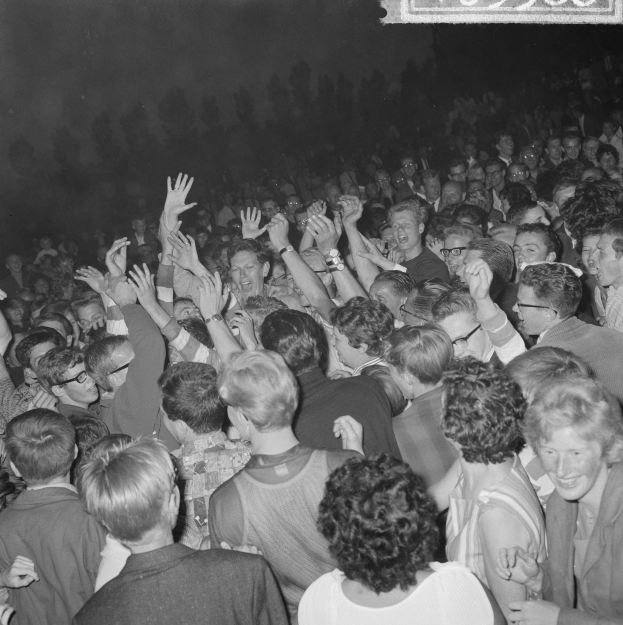 Ein Schwarz-Weiß-Bild einer Menge auf einem Konzert mit erhobenen H├Ąnden um eine Tafel mit Text.