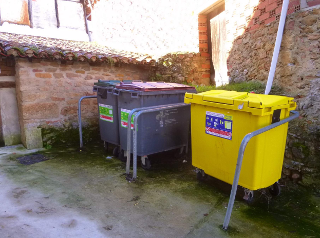 Zwei gelbe und graue Mülltonnen auf Rädern stehen nebeneinander vor einem Gebäude mit einer Wand und einem Fenster im Hintergrund.