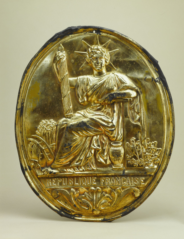 Goldene runde Plakette mit einem Relief der Freiheitsstatue und eingraviertem Text auf weißem Hintergrund.