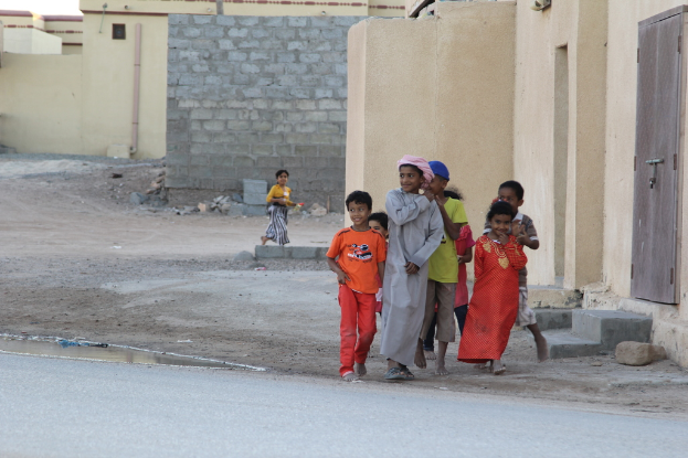 Eine Gruppe lachender Kinder, die vor Gebäuden, Wasser, Felsen und einer Straße steht.