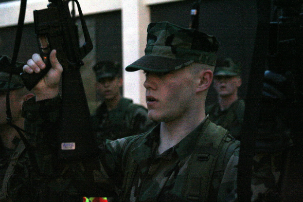 Männer in Uniformen mit Gewehren stehend, mit einer Wand im Hintergrund.