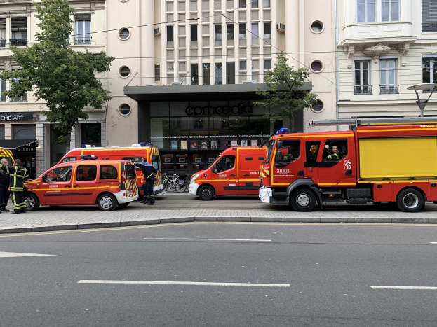 Gruppe von Feuerwehrautos auf einer Straße in Paris geparkt mit Menschen auf dem Bürgersteig, Gebäuden, Bäumen und einem Fahrrad im Hintergrund.