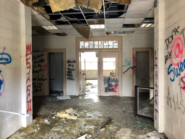 Verlassenes Gebäude mit graffiti-bedeckten Wänden und Decke, Schutt auf dem Boden, mehreren Türen und Fenstern im Hintergrund und verstreuten Gegenständen.