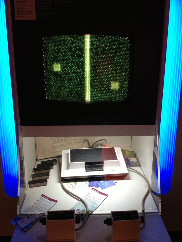 Ein Fernseher steht in einem offenen Schrank umgeben von elektronischen Geräten, Kabeln, Papieren und einem Buch auf einem Tisch, mit sichtbaren Lichtern im Hintergrund.