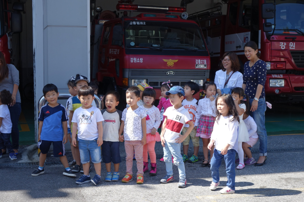 Eine Gruppe von Kindern vor mehreren Feuerwehren auf einem Feuerwehrareal, einige tragen Mützen.