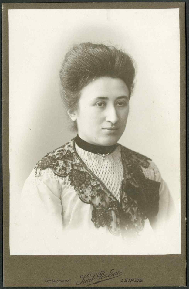 Schwarzes und weißes Foto einer Frau in einem weißen Kleid mit einem gemusterten Schultertuch, identifiziert als Karl Pinkau Leipzig, die direkt in die Kamera schaut.