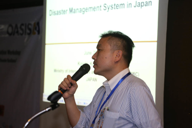 Eine Person mit einem Mikrofon steht vor einer Projektionsfläche, auf der "Notfallmanagementsystem in Japan" steht.
