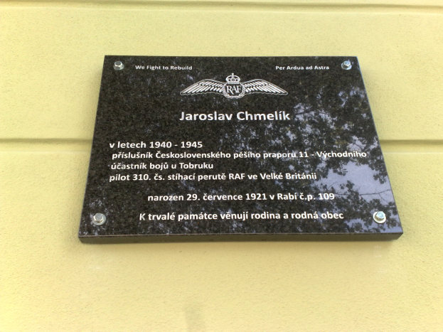Eine schwarze Plakette mit weißer Schrift, die "Jaroslav Chmelik" lautet und von einem dekorativen Rahmen umgeben ist, an einer Gebäudewand angebracht.