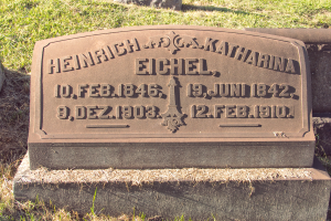 Ein steinernes Grabmal in einem grasbewachsenen Friedhof, mit den Namen Heinrich und Katharina Eichel beschriftet.