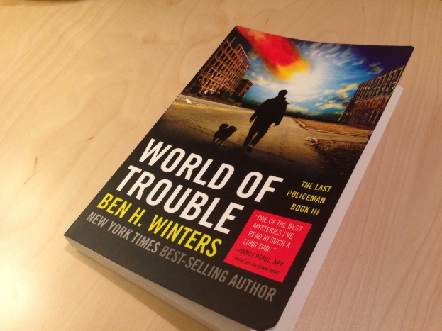 Das Buch "World Of Trouble" wird auf einem Tisch präsentiert, mit einem Coverbild eines Mannes und eines Hundes.