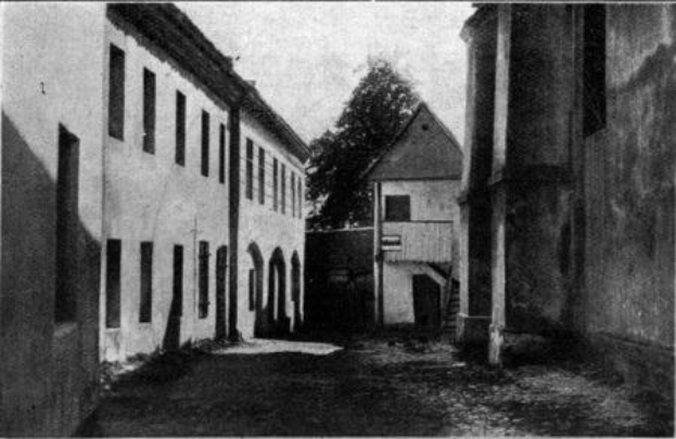 Schwarz-weiß-Foto eines ehemaligen Gefängnisses in Stuttgart, Deutschland, mit Fenstern, einem Baum und Himmel im Hintergrund, mit Text unten, das es als "Grundfosz" identifiziert