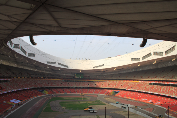 Großes Stadion mit Zuschauern auf den Rängen, Fahrzeugen unten, Strommasten und einem Schuppen oben, vor einem Himmel als Hintergrund.