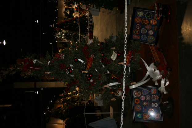 Ein Weihnachtsbaum mit Geschenken, Rahmen und Spielzeugen auf einer Plattform, mit Menschen, zusÃ¤tzlichen WeihnachtsbÃ¤umen und Deko im Hintergrund.