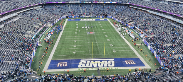 Ein Fußballstadion voller Zuschauer, Spieler und verschiedener Gegenstände auf dem Feld, umgeben von Stühlen und Tafeln mit Text.