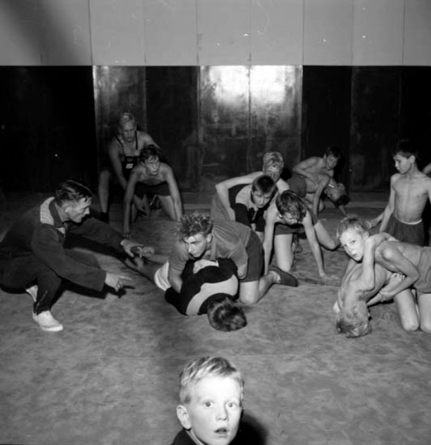 Eine Gruppe junger Jungs ringt in einem schwarz-weißen Gym, mit einer Wand im Hintergrund.