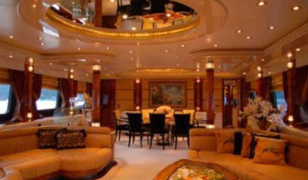 Ein Hotellobby mit Sofas, Stühlen, Tischen und Dekorationsgegenständen im Vordergrund, Fenstern mit Vorhängen und Lampen auf beiden Seiten, einem gerahmten Bild und einer Leuchte im Hintergrund und einem Spiegel mit Deckenleuchten oben.