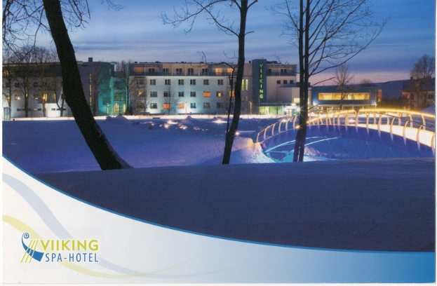 Winterszene eines Wikinger-Spa-Hotels mit schneebedecktem Boden, einer beleuchteten Brücke, Bäumen, Gebäuden mit Fenstern und einem bewölkten Himmel, mit Text auf der linken Seite.