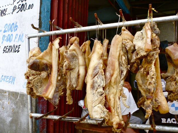 Fleisch, das an einem Ständer hängt, mit einer Person dahinter und einer Wand mit Text auf der linken Seite.
