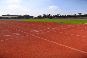 Laufbahn mit Bahnnummern, umgeben von grünem Gras und Bäumen, mit einem Stadion und einem klaren blauen Himmel im Hintergrund.