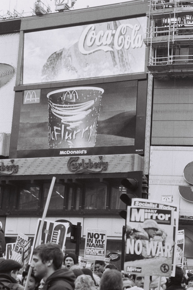 Menschen mit Plaketten vor Gebäuden.