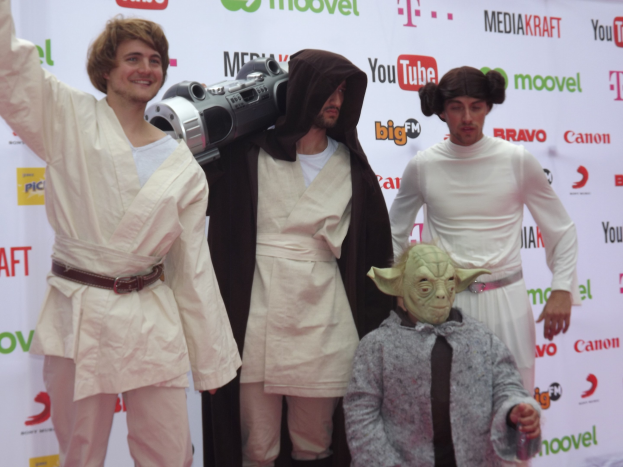 Eine Gruppe von Menschen in Star-Wars-Kostümen, die auf einem roten Teppich posieren und im Hintergrund ein Banner zu sehen ist.