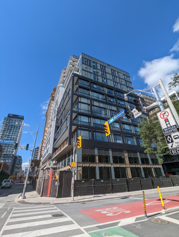 Eine belebte Stadtstraße mit hohen Gebäuden, Fahrzeugen, Verkehrszeichen, Schildern, Bäumen, einem Zaun und einem bewölkten Himmel, mit einem zum Verkauf stehenden Apartment/Wohnhaus in 541 East 57th Street, Unit 541.