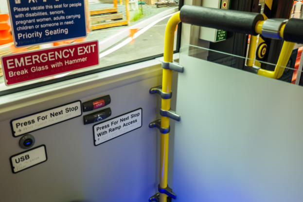 Notausgangsschild an der Seite eines Zuges, mit einer Tür mit Griff im Vordergrund und einem Glasfenster, das die Straße, Pfähle und andere Gegenstände draußen zeigt.