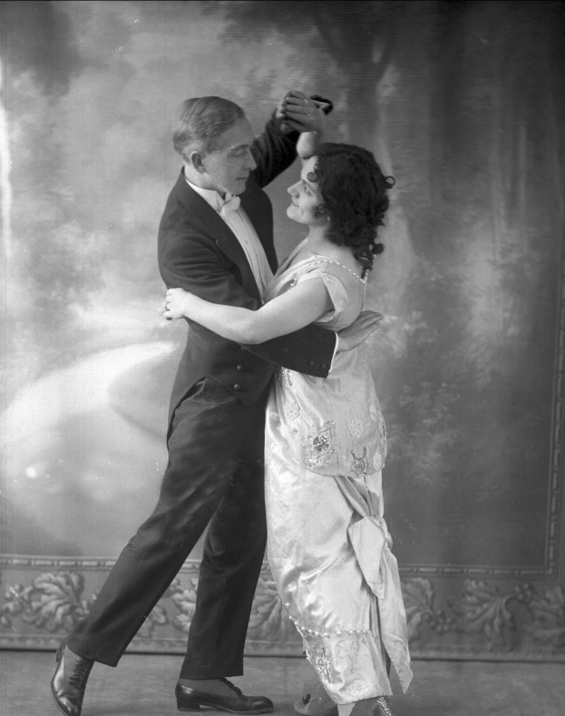 Schwarz-weiß-Foto eines Mannes in einem Anzug und einer Frau, die Tango tanzen, mit kunstvollen Wanddesigns im Hintergrund.