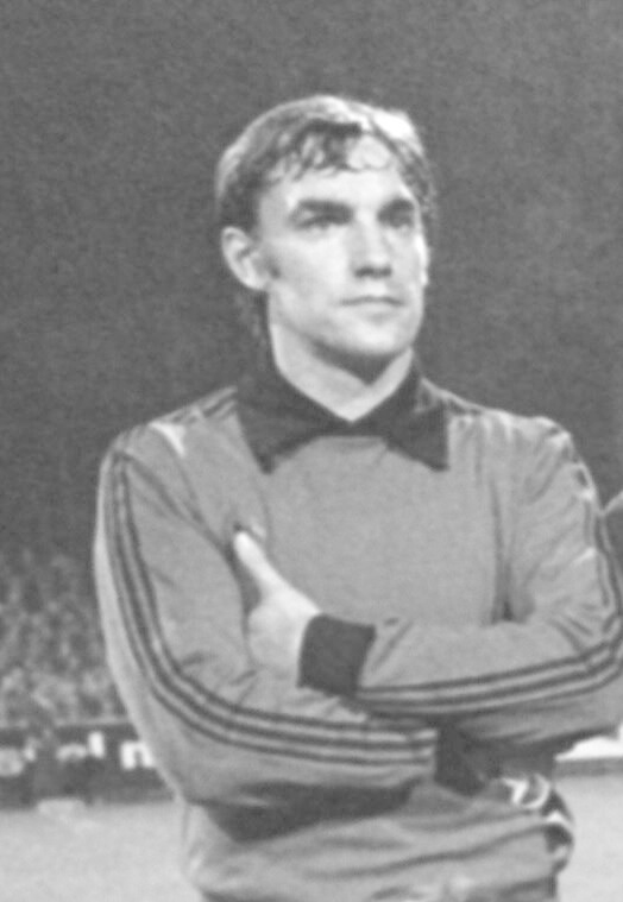 Schwarzes und weißes Foto eines Mannes, der mit verschränkten Armen auf einem Fußballfeld steht und von sitzenden Zuschauern umgeben ist, der als legendärer Torwart von Manchester United gilt, der im Alter von 89 Jahren verstorben ist.