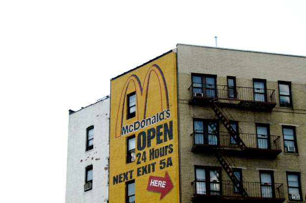Ein Geb├Ąude mit Text und einer Wandmalerei, das Treppen, Gel├Ąnder, Klimaanlagen an den Fenstern und ein Rohr ├╝ber dem Himmel zeigt.