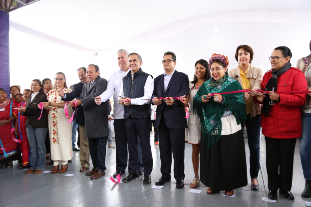 Eine Gruppe von Menschen hält eine Schere vor einer Menge, mit Papieren auf dem Boden und einem weißen Tuch im Hintergrund.