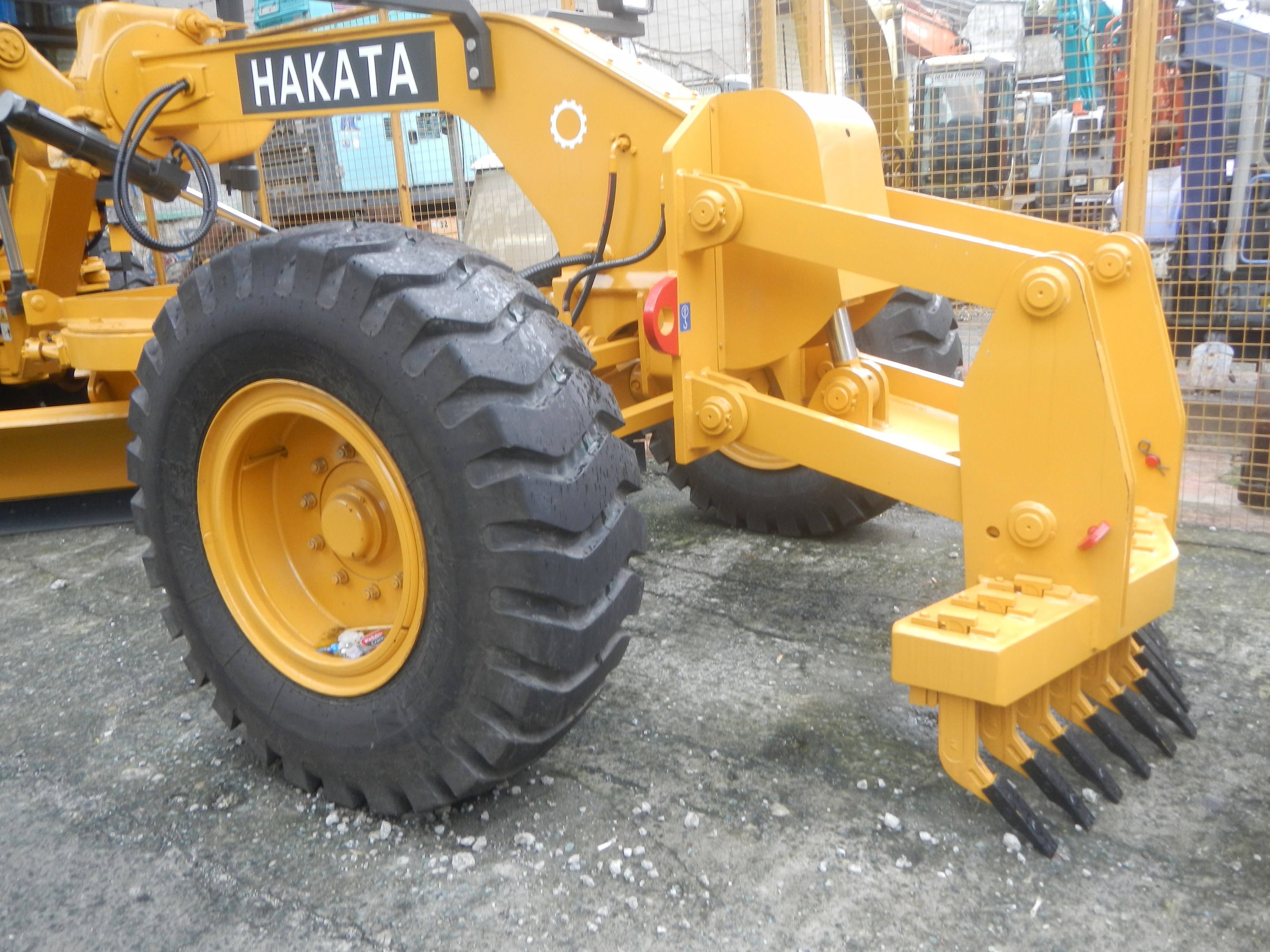 Ein gelber Radlader steht vor einem Gebäude mit einem Metallzaun und einem klaren blauen Himmel im Hintergrund.