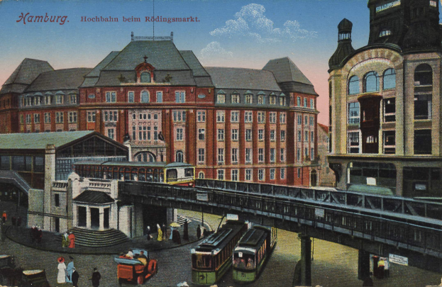 Eine alte Postkarte zeigt einen Bahnhof in Hamburg, Deutschland, mit Menschen, Fahrzeugen, einer Brücke, Gebäuden und einem bewölkten Himmel sowie Text oben.